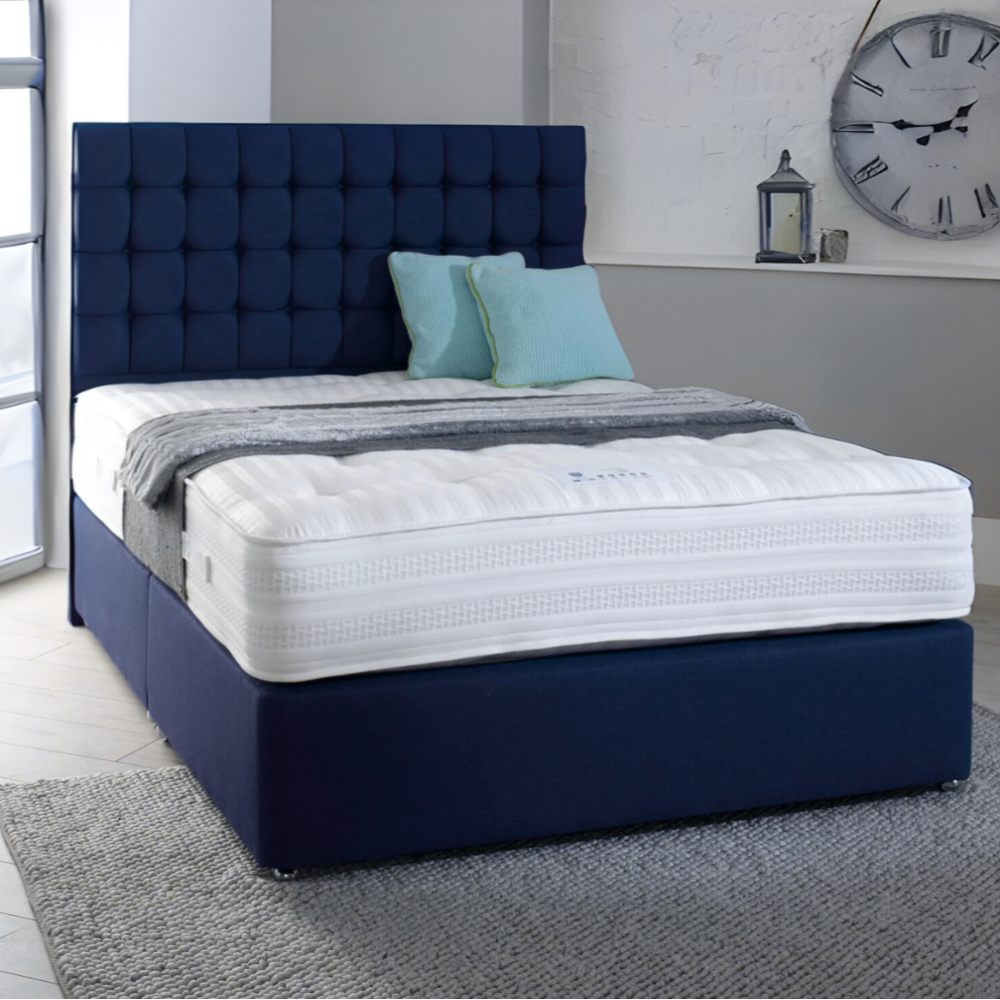 A bedroom with a navy blue MarioCubeBed, white mattress, teal pillows, and a gray blanket, with a large wall clock and a lantern on a mantle nearby.