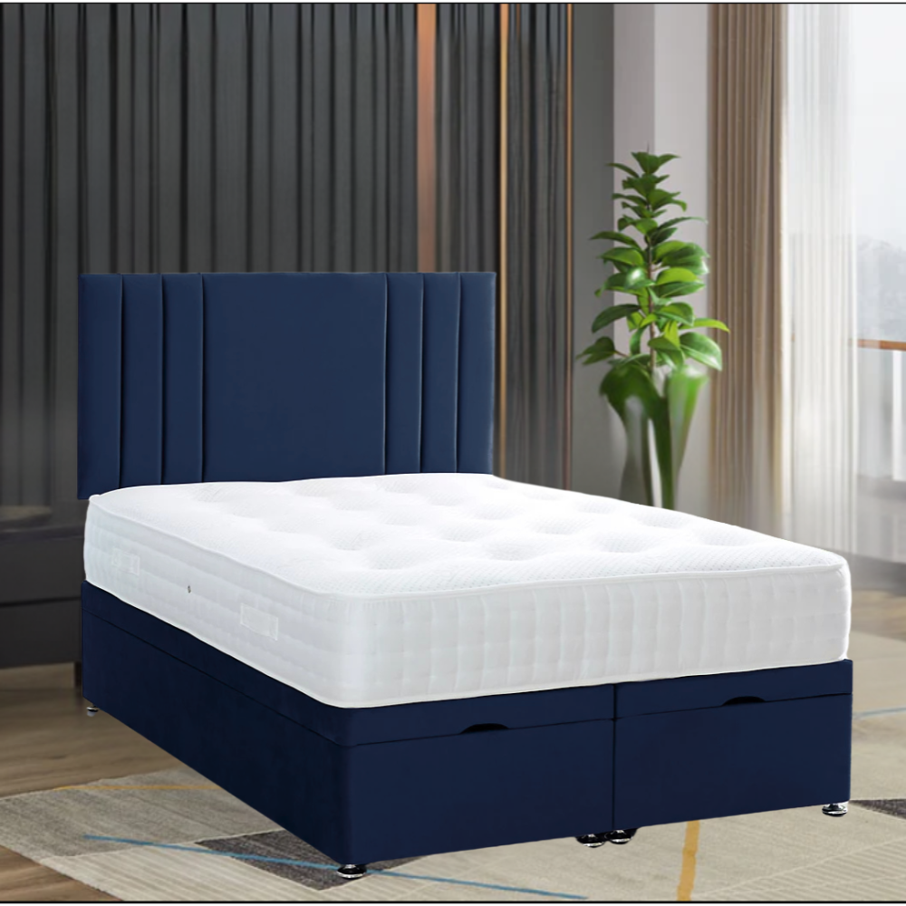 A RowanPanelBed with a deep blue upholstered headboard and a white quilted mattress, set in a modern room with curtains and a green plant.