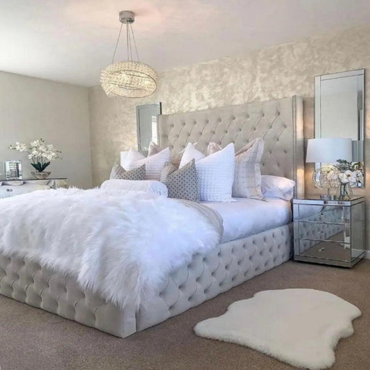 Elegant bedroom with tufted Eva Wingback Bed, plush bedding, and a mirrored nightstand under a decorative chandelier.