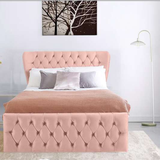 A pink tufted EvelynWingbackBed  with multi-colored pillows and a beige blanket, underneath a tree painting, next to a floor lamp.

