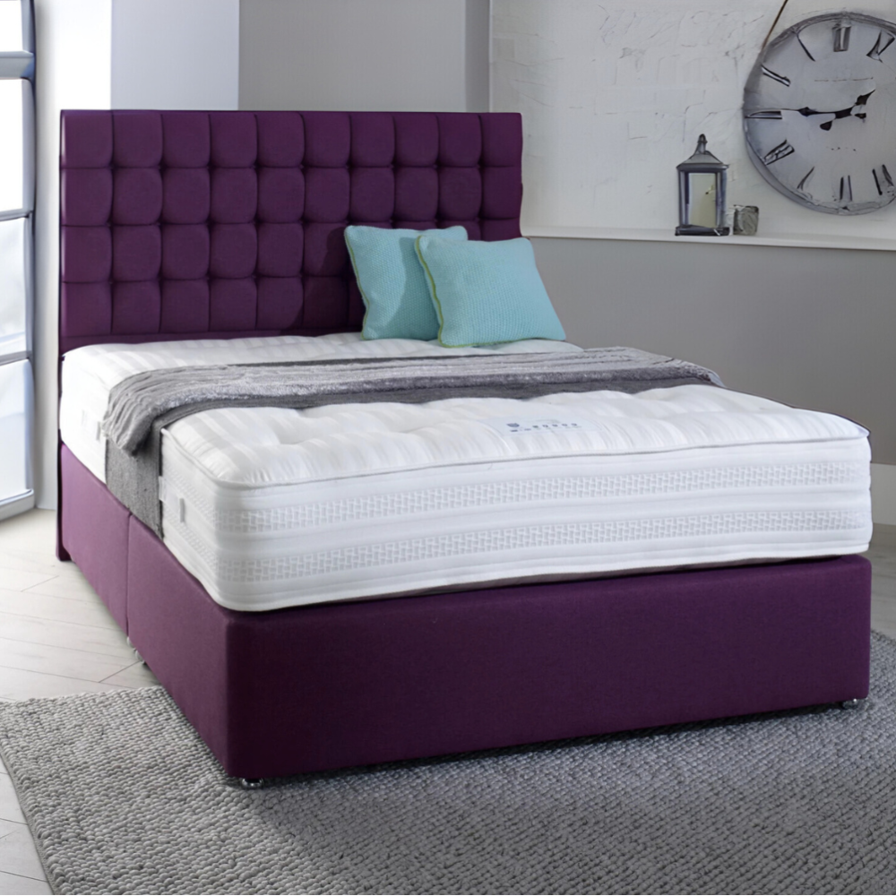 A MarioCubeBed with a tufted purple headboard and a white mattress, featuring light blue pillows and a gray blanket.

