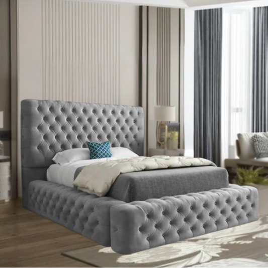 A modern bedroom with a gray tufted  MillyAmbassadorbed, white bedding, and a blue decorative pillow.

